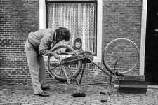 830216 Afbeelding van een bewoner van de De Kockstraat (Zeven Steegjes) te Utrecht die zijn fiets repareert.